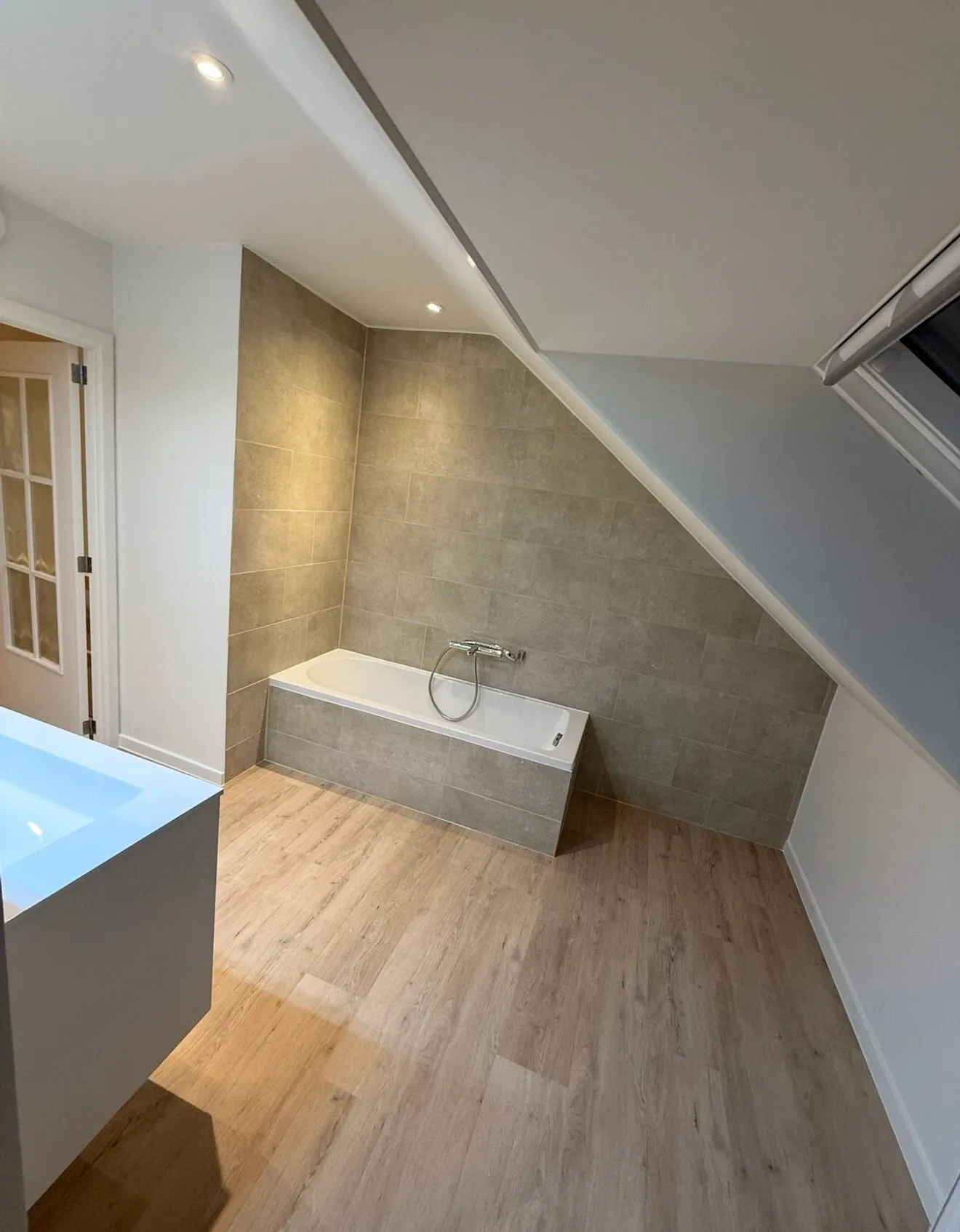 Afgewerkte badkamer met ingewerkt ligbad onder een schuin dak