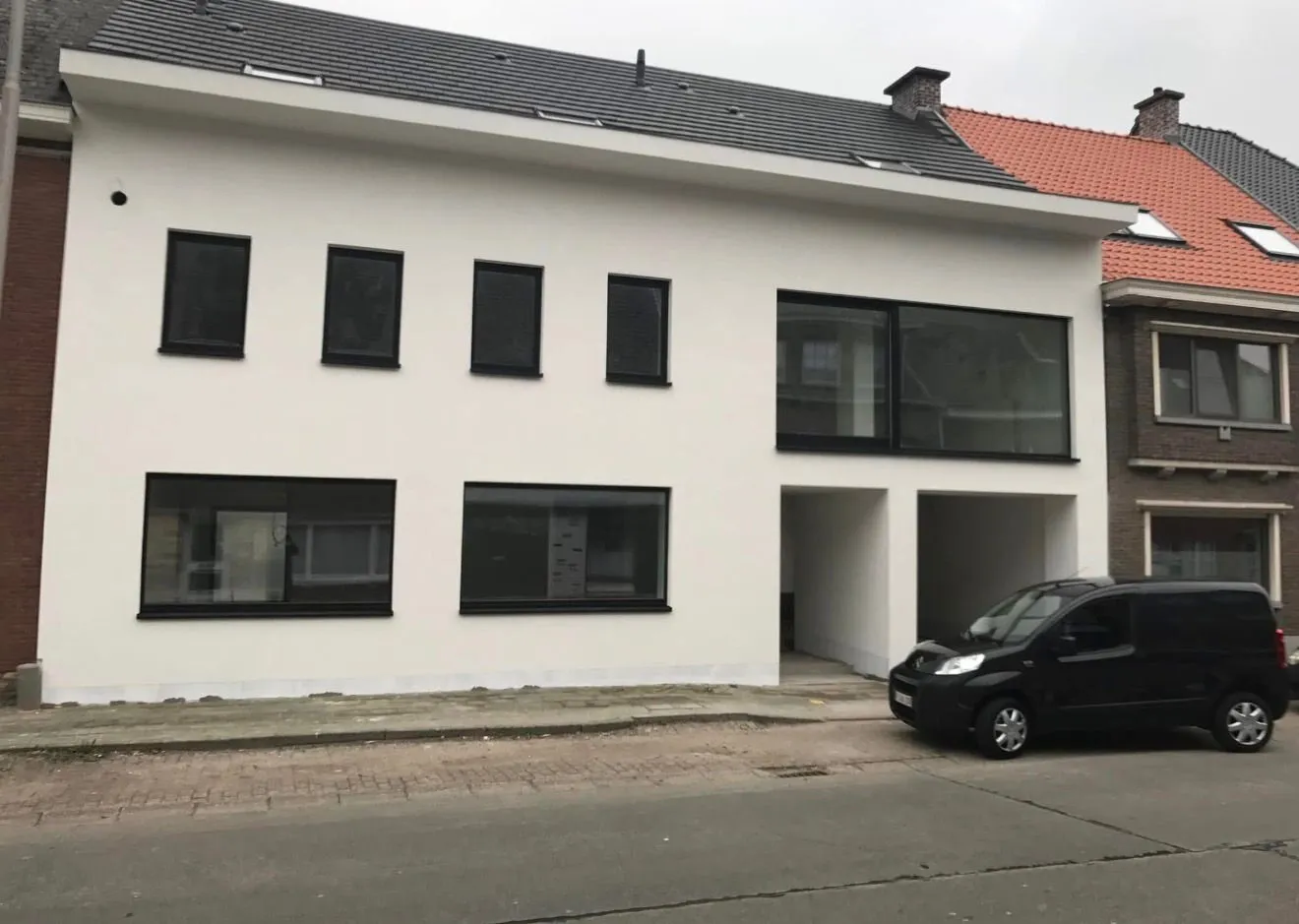 Woning met strakke witte crepi-afwerking en zwart schrijnwerk