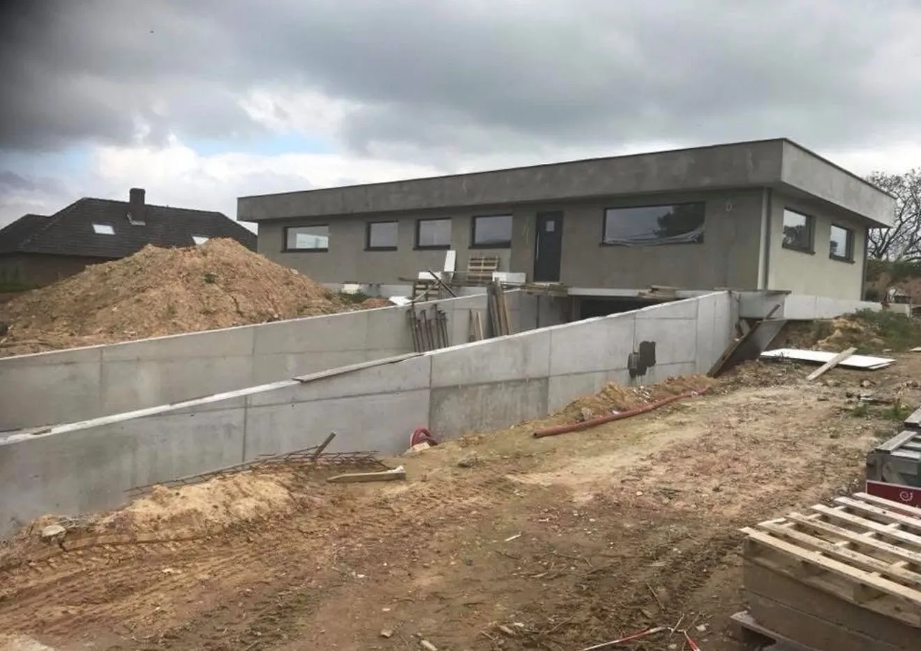 Ruwbouw van een nieuwbouwwoning met betonnen keermuur en grondwerken