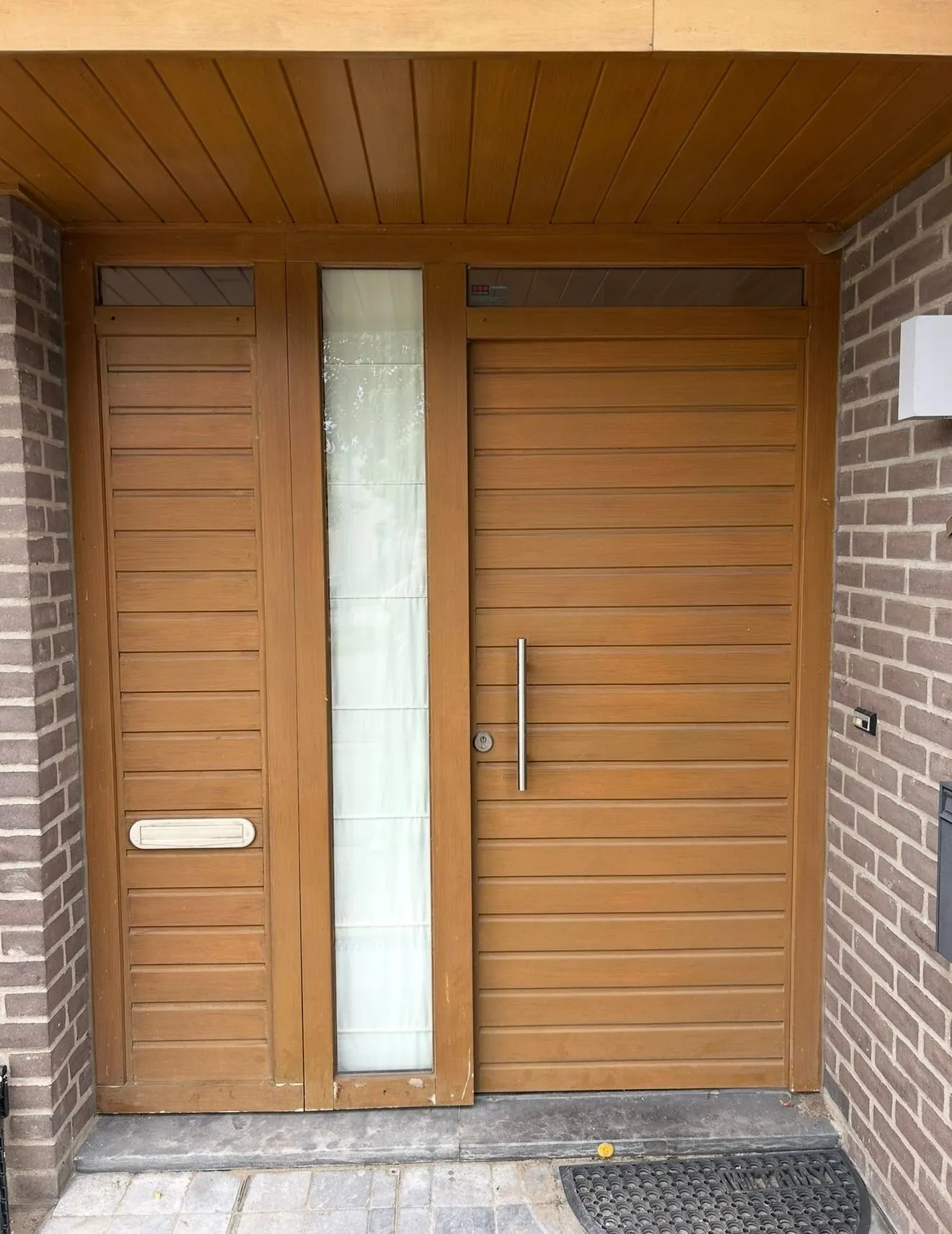 Nieuwe houten voordeur met zijlicht en houten luifel